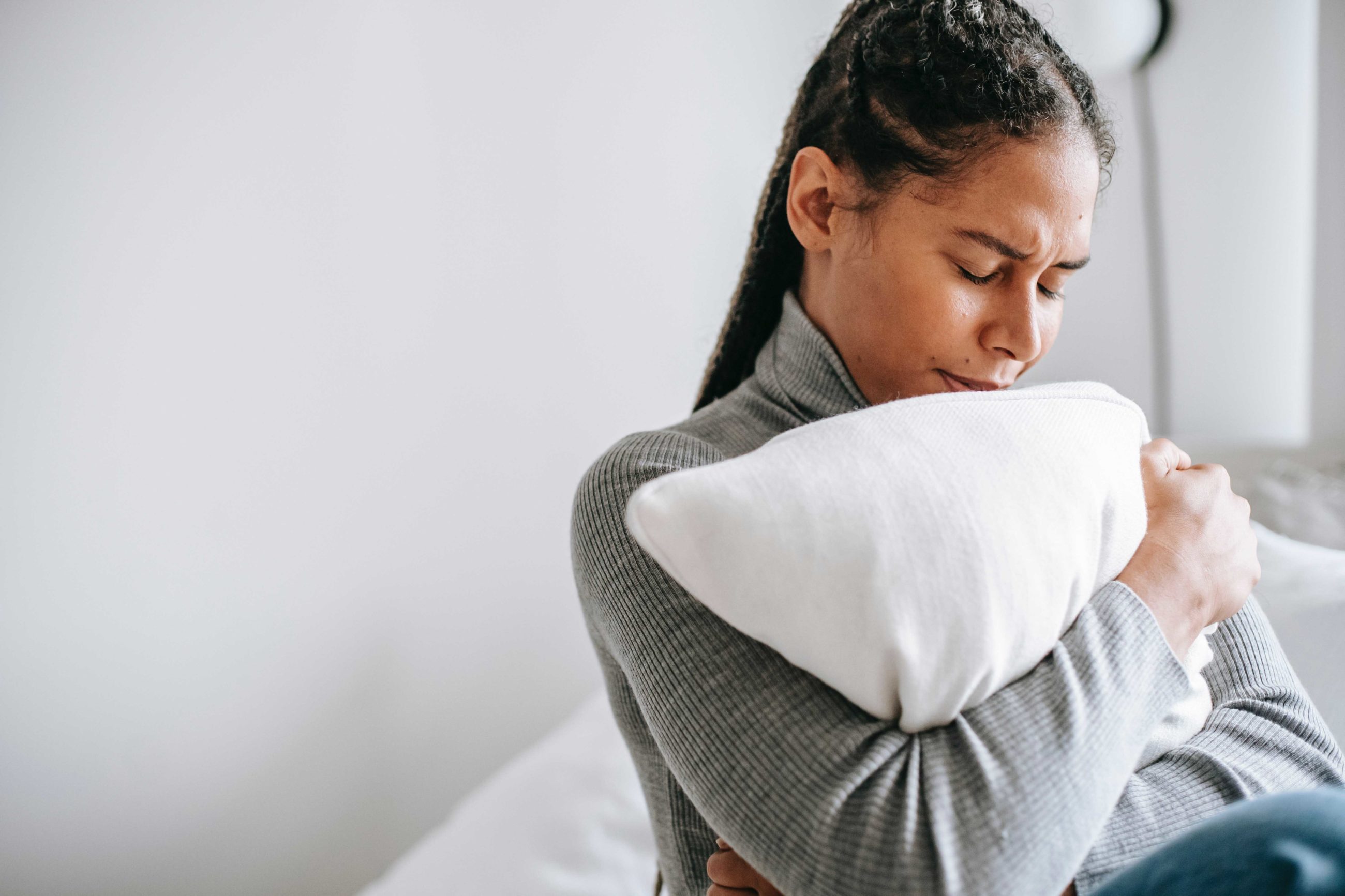 Sad woman on a bed holding a cushion against her